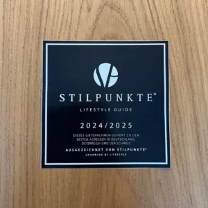 Stilpunkte Lifestyle Guide 2024/2025 Auszeichnung. Das Bild zeigt ein quadratisches Schild mit schwarzem Hintergrund, auf dem in weißer Schrift steht: ‘STILPUNKTE LIFESTYLE GUIDE 2024/2025. Dieses Unternehmen gehört zu den besten Adressen in Deutschland, Österreich und der Schweiz. Ausgezeichnet von Stilpunkte® - Charming by Lifestyle.’