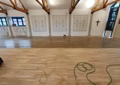 Renovierter Parkettboden im Pfarrheim Korschenbroich mit sichtbaren Kabeln und Holzstruktur.
