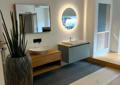 Ausgestellte maßgefertigte Badezimmermöbel mit modernem Waschtisch, beleuchtetem Rundspiegel und Badschrank in der Ausstellung von Tischlerei Daniel Albani in Korschenbroich.